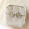 The stamped flower peridot post earrings styled on a white velvet box