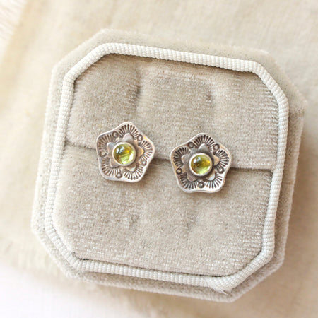 The stamped flower peridot post earrings styled on a white velvet box