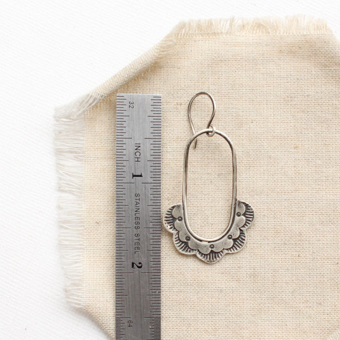 A columbine hoop earring next to a ruler for size reference