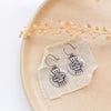 The layered soar earrings styled on a tan plate with linen and dried grass