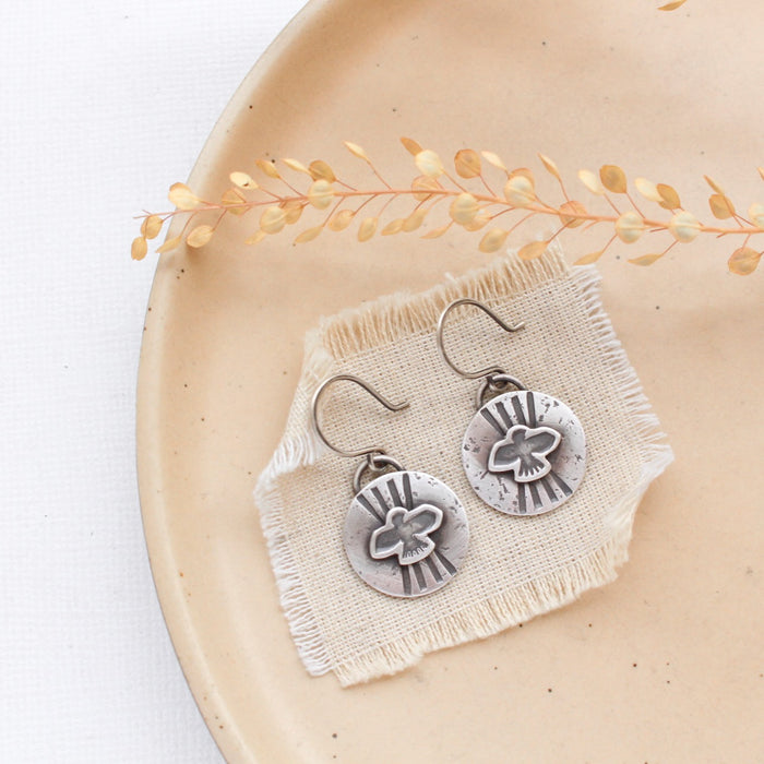 The layered soar earrings styled on a tan plate with linen and dried grass