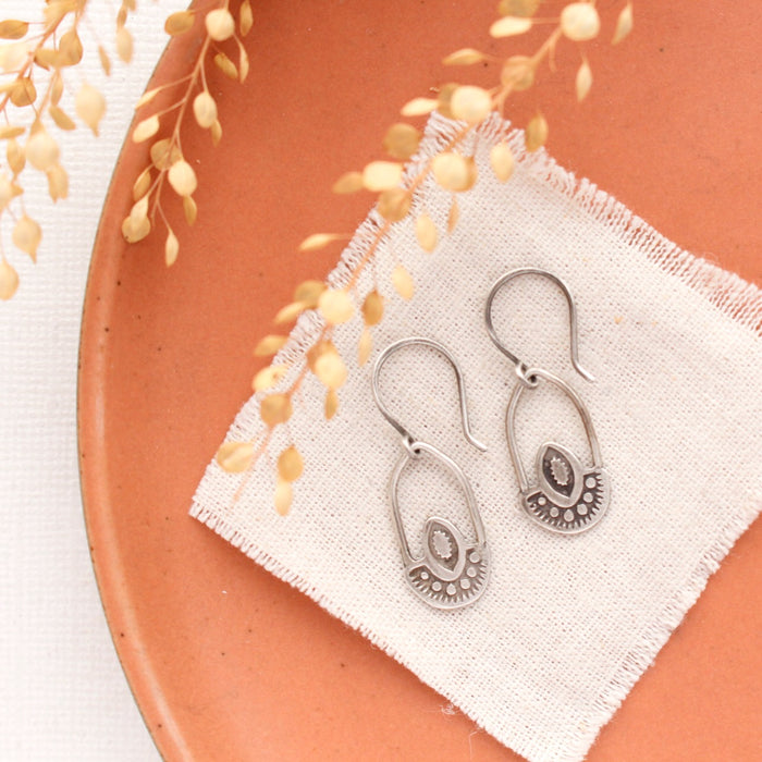 The wanderer hoop earrings styled on an orange plate with linen and dried grass