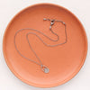 The wanderer hoop necklace styled on an orange plate to show the adjustable lobster clasp closure