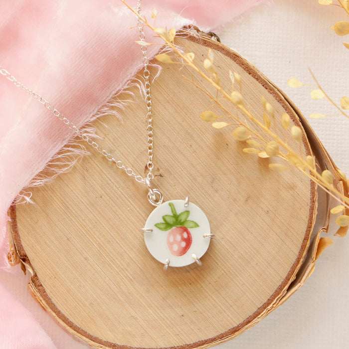 The strawberry bud vintage plate necklace styled on wood with pink velvet and dried grass