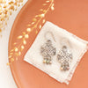 The sun cross rainbow agate earrings styled on an orange plate with linen and dried grass