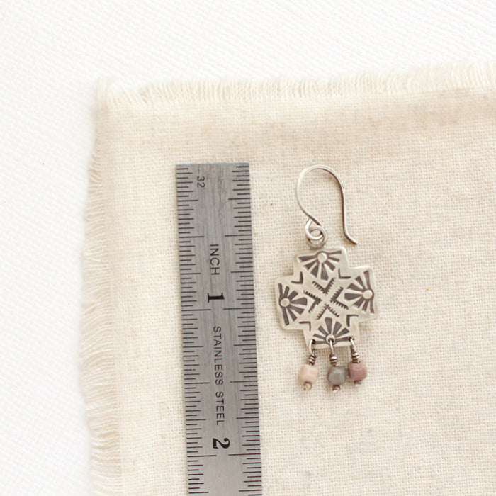A sun cross rainbow agate earring next to a ruler for size reference