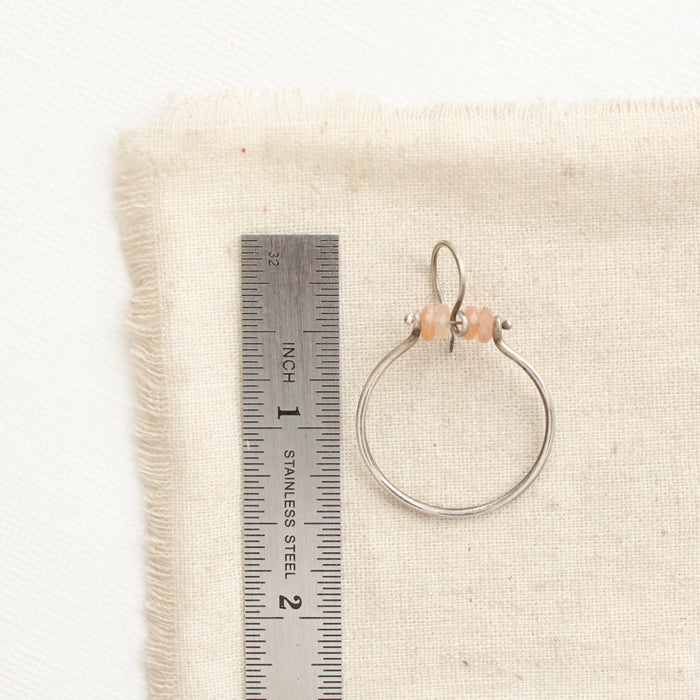 A sunstone halo hoop earring next to a ruler for size reference