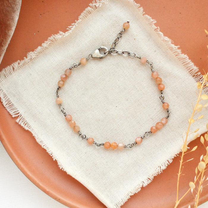 The wrapped sunstone bracelet styled on an orange plate with tan linen and dried grass
