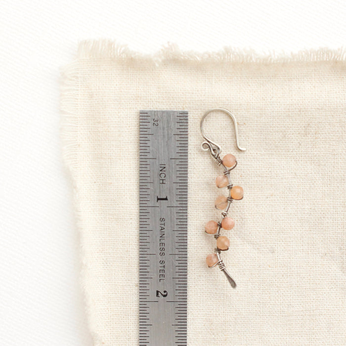 A sunstone wrapped silver vine earring next to a ruler for size reference