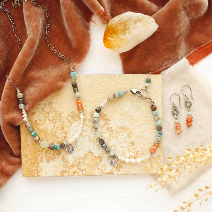 The talara sun mesa necklace, earrings, and bracelet styled on a tan rock with orange velvet and a crystal