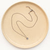 The mini talara sun necklace styled on a tan plate to show the adjustable clasp closure