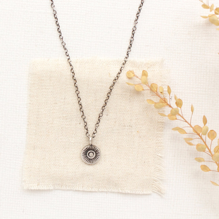 The talara sun necklace styled on tan linen with dried grass