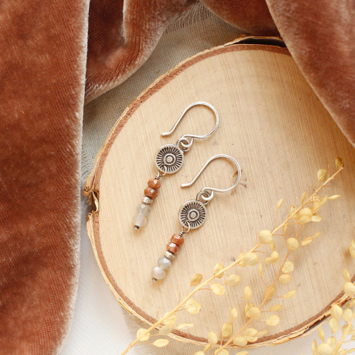 The talara sun zaria earrings styled on wood with brown velvet and dried grass