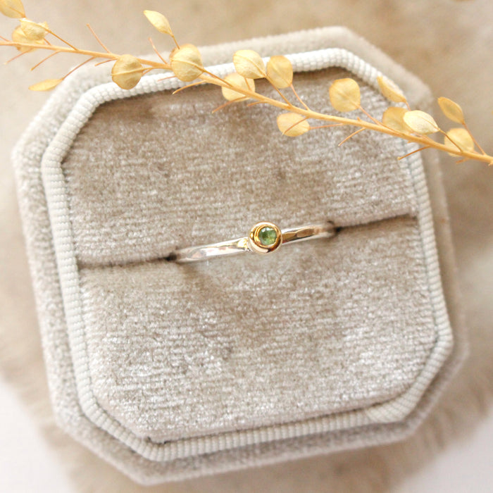 The green tsavorite garnet mixed metal stacked ring styled on a beige velvet ring box with tan linen and dried grass