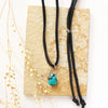 The turquoise drop adjustable leather necklace styled on a tan rock with dried grass