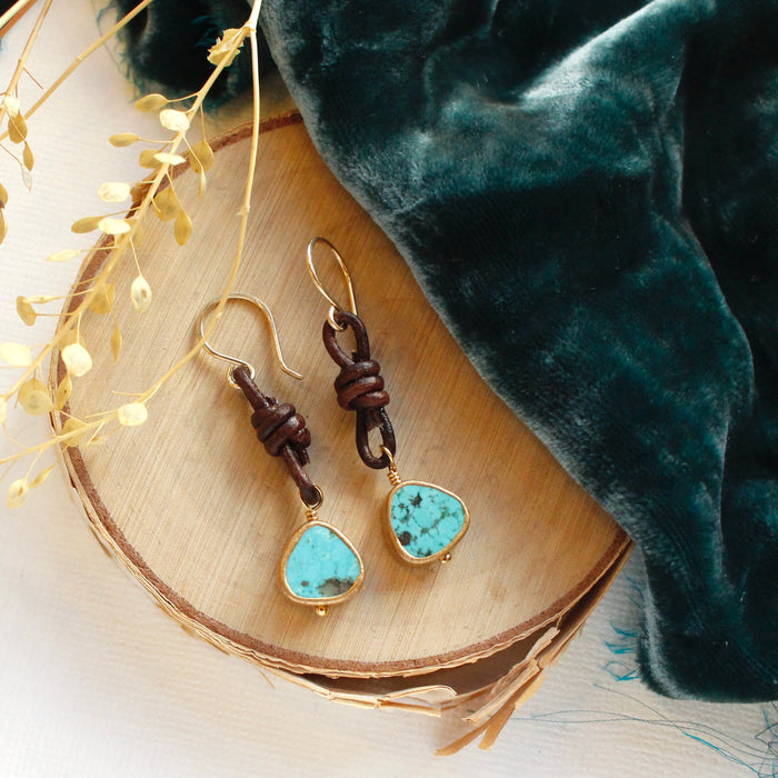 The turquoise and leather earrings styled on wood with blue velvet and dried grass