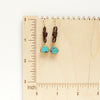 The turquoise and leather earrings on a wooden ruler for size reference