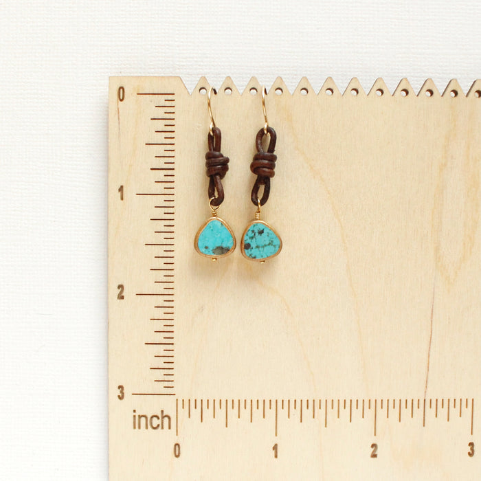 The turquoise and leather earrings on a wooden ruler for size reference