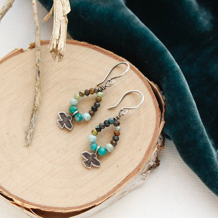 The serenity soar hoop earrings styled on wood with blue velvet and dried grass
