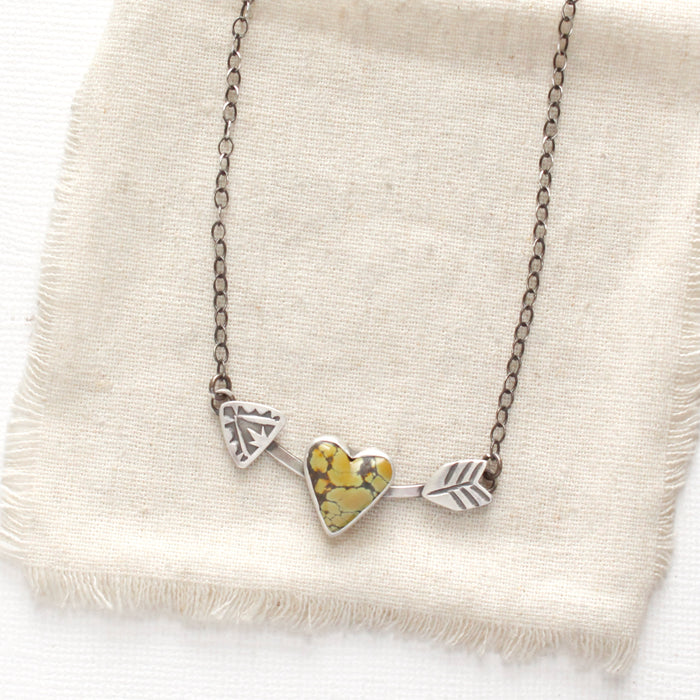 The cupid's arrow necklace styled on tan linen