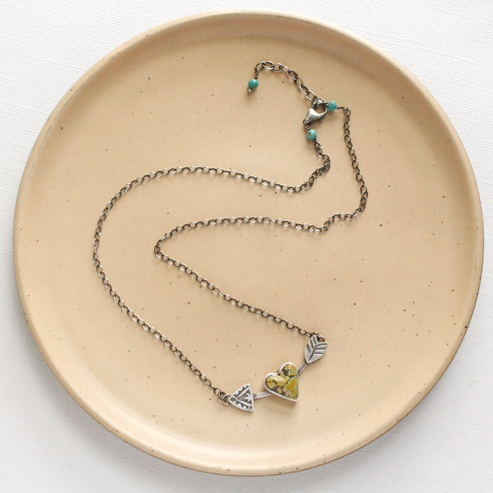 The cupid's arrow necklace styled on a tan plate to show the adjustable lobster clasp closure