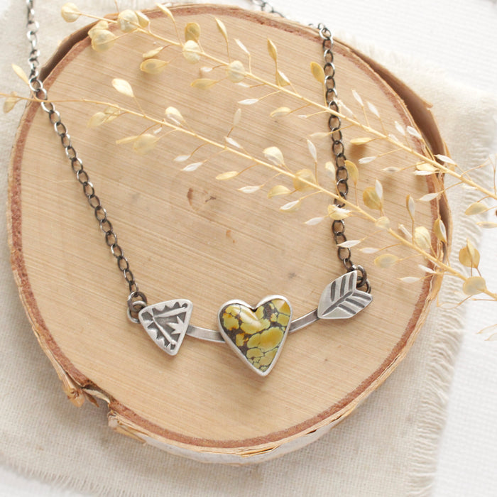 The turquoise cupid's arrow necklace styled on wood with linen and dried grass