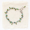 A bracelet made of turquoise cubes and dangling chrome diopside styled on tan linen.