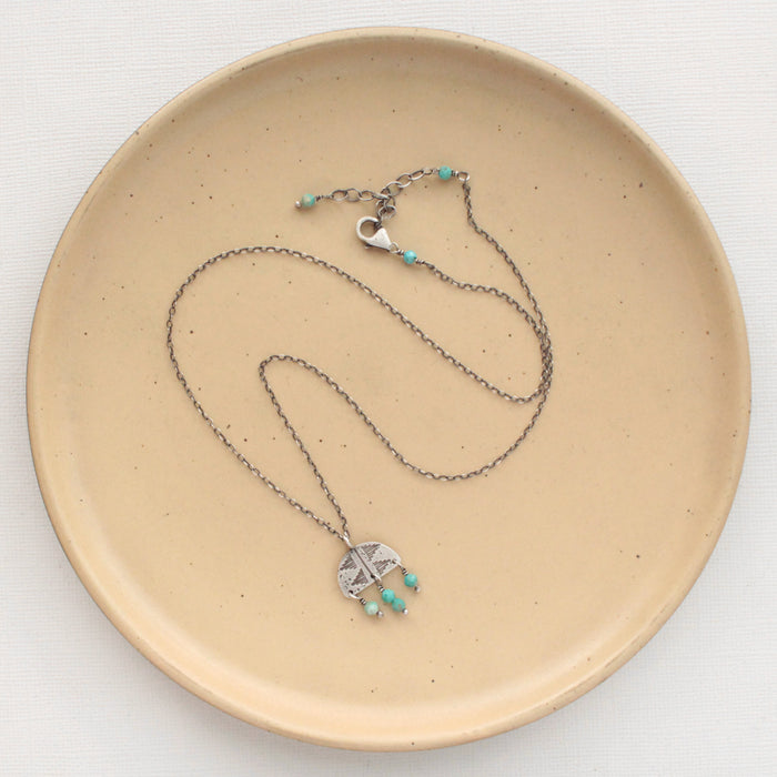 The turquoise fringe pakal arch necklace styled on a tan plate to show the adjustable lobster clasp closure