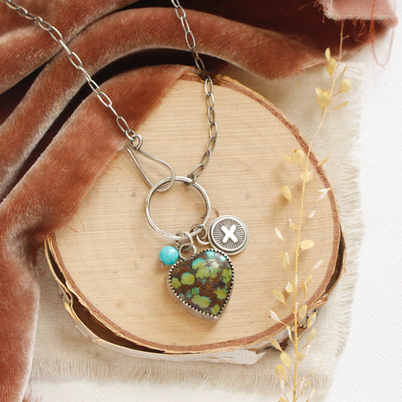 The royston turquoise charm necklace styled on wood with brown velvet and dried grass