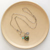 The royston turquoise heart charm necklace styled on a tan plate to show the the entire chain