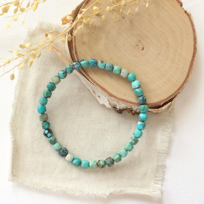 The turquoise cube stretch bracelet styled on wood with linen and dried grass