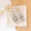 The wanderer arch mixed metal labradorite earrings styled on linen with dried grass