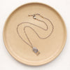 The wanderer arch mixed metal labradorite necklace styled on a tan plate to show the adjustable lobster clasp closure