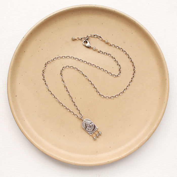 The wanderer arch mixed metal labradorite necklace styled on a tan plate to show the adjustable lobster clasp closure