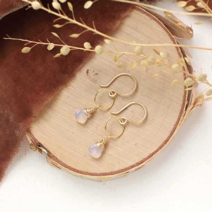 The white opal drop hoop earrings styled on wood with orange velvet and dried grass