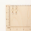 The white opal hoop earrings on a wooden ruler for size reference