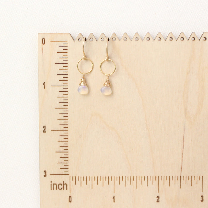 The white opal hoop earrings on a wooden ruler for size reference