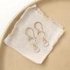 The white opal gold hoop earrings styled on a tan plate with linen