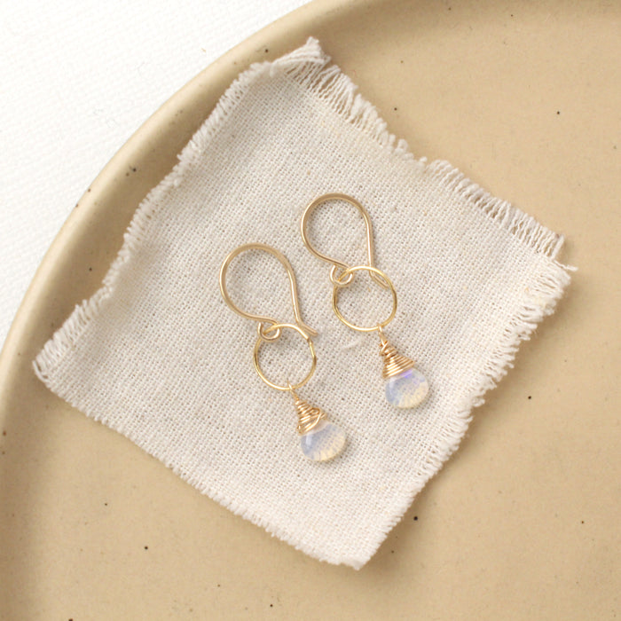 The white opal gold hoop earrings styled on a tan plate with linen