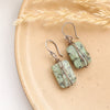 The wrapped african jasper earrings styled on a tan plate with dried grass