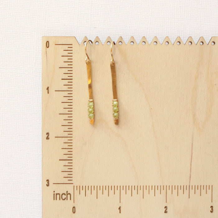 The peridot wrapped gold bar earrings on a wooden ruler for size reference