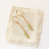 The peridot wrapped gold bar earrings styled on tan linen