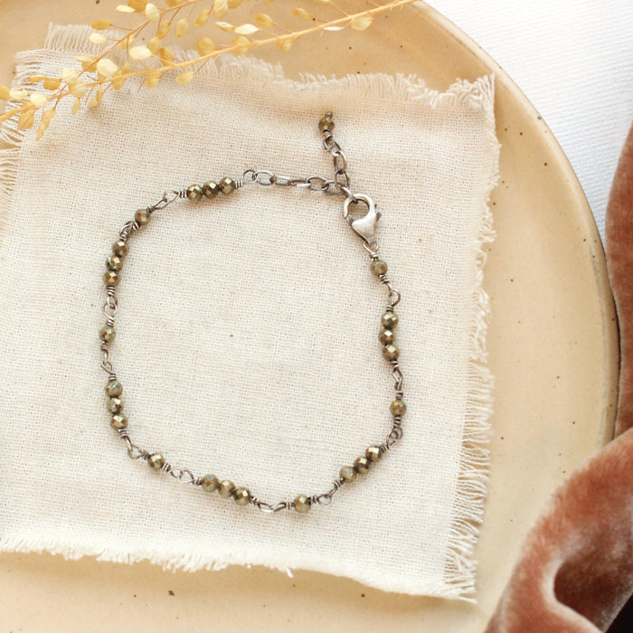 The wrapped pyrite bracelet styled on a tan plate with linen and dried grass