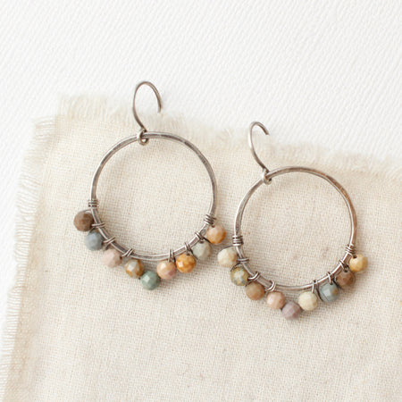The wrapped rainbow agate hoop earrings styled on tan linen