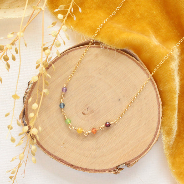 The wrapped rainbow necklace styled on wood with yellow velvet and dried grass