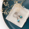 The silver wrapped turquoise earrings styled on a blue plate with linen and dried grass