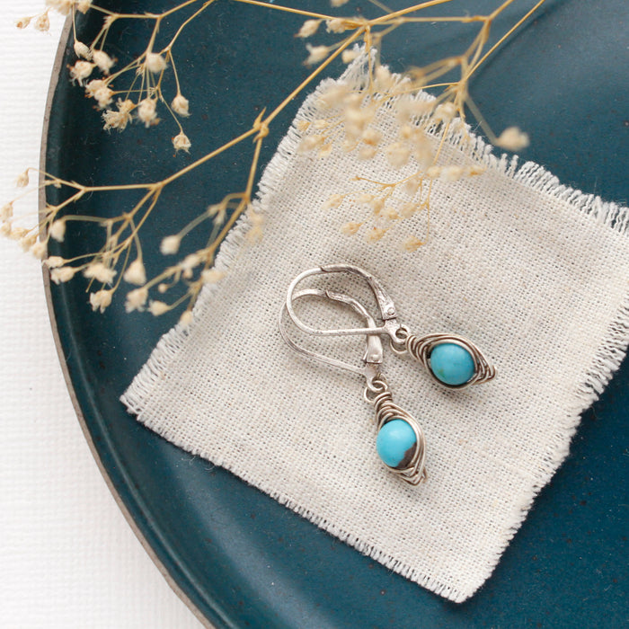 The silver wrapped turquoise earrings styled on a blue plate with linen and dried grass