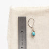 A silver wrapped turquoise earring next to a ruler for size reference