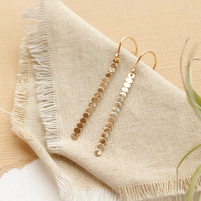 The yellow gold beaded bar earrings styled on tan linen with an air plant