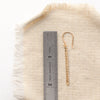 A yellow gold beaded bar earring next to a ruler for size reference